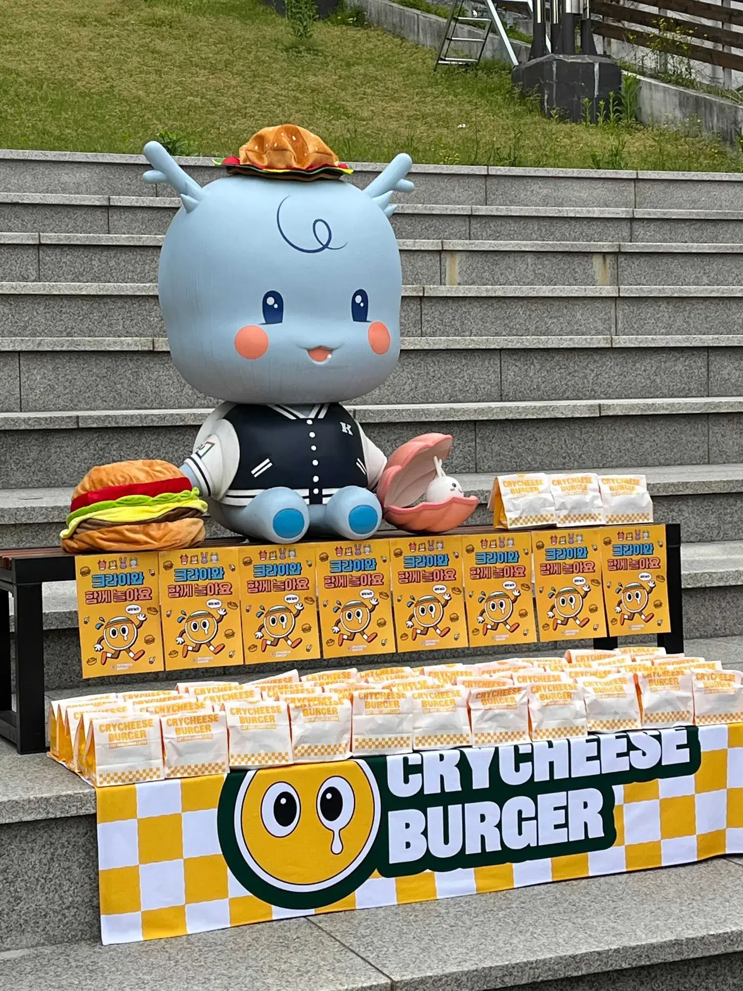 야외 계단에 학교 마스코트 인형과 버거 봉투를 차린 부스