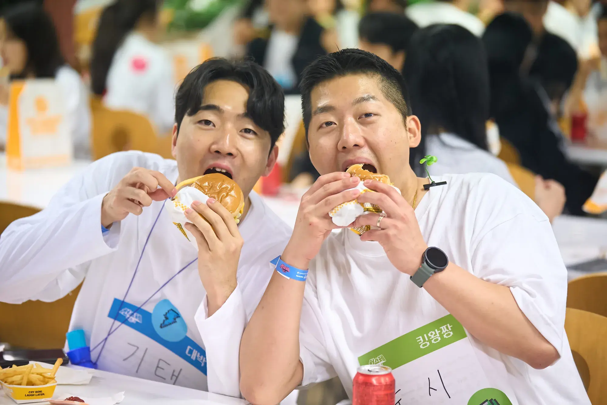 행사장에서 버거를 크게 한 입 베어 무는 참가자 두 명